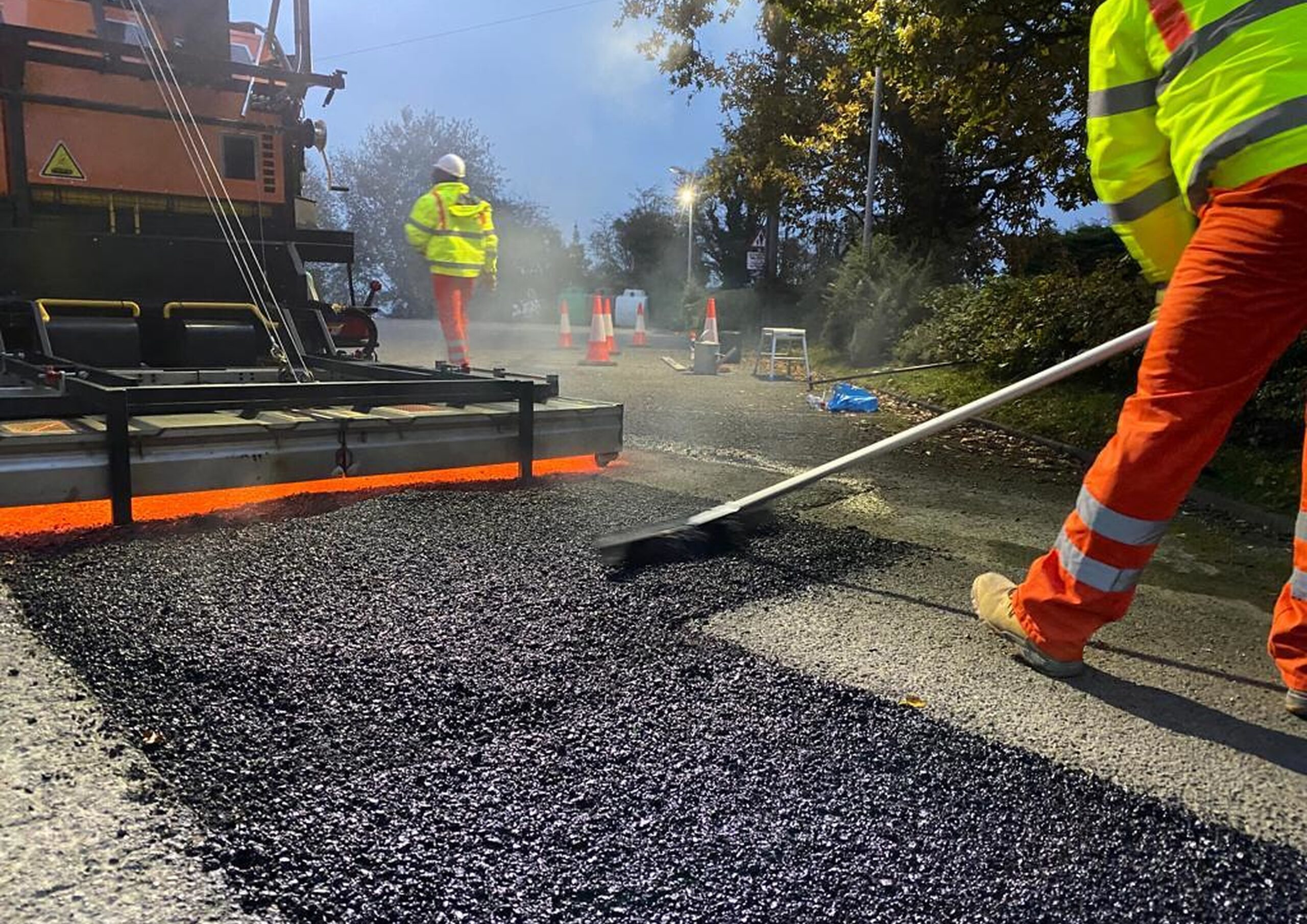 Road workers laying hot asphalt during road surface repair using asphalt patching machines SILKOT and hand tools.