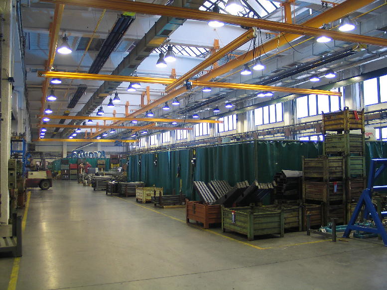 Tmavé plynové infražiariče KM-U v priemyselnej výrobnej hale s mostovým žeriavom.