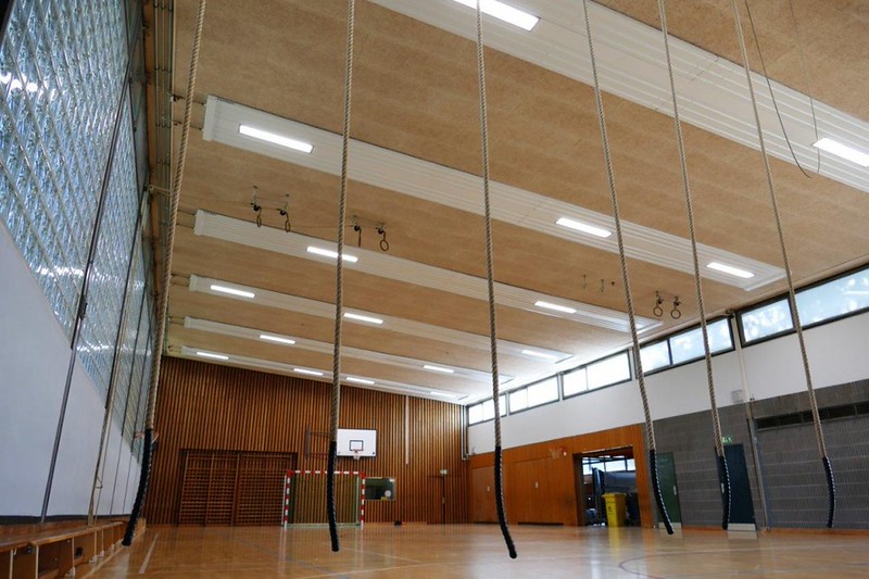 Radiant panel with integrated LED lighting suspended beneath the ceiling of a sports hall.